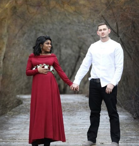 A black woman in a red dress poses with her white male interracial partner, dressed in black pants with a white collared shirt